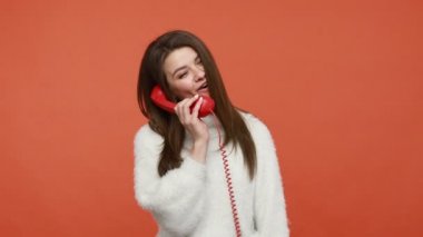 Tüylü, beyaz kazaklı, elinde kırmızı bir cep telefonuyla konuşan, iletişimi koparmayan, sohbet eden pozitif bir esmer kadın. Turuncu arka planda kapalı stüdyo çekimleri
