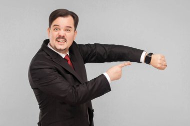 Fazla zamanımız yok, acele edin lütfen! Kapalı stüdyo çekimi. Gri arka planda izole. Siyah takım elbiseli, kırmızı kravatlı ve bıyıklı yakışıklı işadamı kameraya bakıyor..