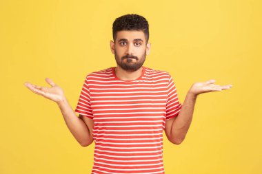 Çizgili kırmızı tişörtlü, sakallı, elleri açık, omuzlarını silkmiş, emin olmayan ve bazı sorulara kayıtsız kalmış budala bir adam. Sarı arka planda kapalı stüdyo çekimleri