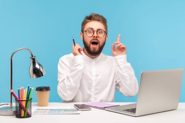 Heyecanlı adam ellerini kaldırıyor ve kameraya geniş açık gözler ve ağızla bakıyor, eureka, başlamak için iyi bir fikri var, ilham. Mavi arka planda kapalı stüdyo çekimi