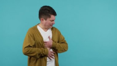 Karnım ağrıyor. Beyaz tişörtlü, karnı ağrıyan, karnı şişmiş, gastrit veya pankreas iltihabı olan orta yaşlı hasta bir adam. Mide ekşimesi. Mavi arka planda kapalı stüdyo çekimi