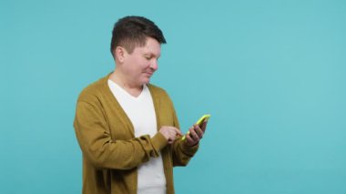 Çevrimiçi mobil iletişim. Yetişkin, koyu renk saçlı, mesaj yazan, sosyal ağda cevap üzerinde düşünen, akıllı telefondan mesaj atan, flört uygulaması ile sohbet eden bir adam. Mavi arka planda kapalı stüdyo çekimi