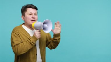 Ciddi, olgun, esmer adam yüksek sesle konuşuyor, megafonu ağzının kenarında tutuyor, açıklamaya çalışıyor, bakış açısını ifade ediyor, duyuru yapıyor. Mavi arka planda kapalı stüdyo çekimi
