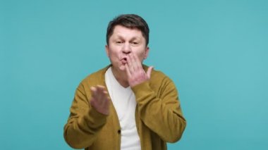 Beyaz tişörtlü ve hırkalı mutlu, koyu renk saçlı bir adam bir sürü hava öpücüğü gönderiyor kameraya bakıyor ve gülümsüyor, seninle flört ediyor. Mavi arka planda kapalı stüdyo çekimi