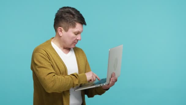 プロファイルの肖像画白いTシャツとカーディガンの手にそれを保持ノートパソコンを入力して深刻なブルネット成熟した男は スタートアッププロジェクトに取り組んで 行うにはリストを作る 青い背景に隔離された屋内スタジオショット — ストック動画