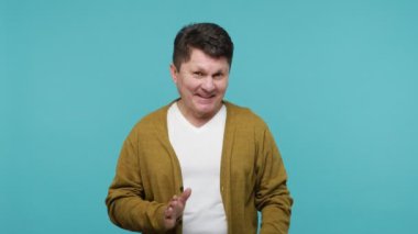 Beyaz tişörtlü ve hırkalı komik, kurnaz, olgun bir adam kameraya sinsi bir ifadeyle bakıyor dolambaçlı hileler ve planlar yapıyor, eğleniyor. Mavi arka planda kapalı stüdyo çekimi