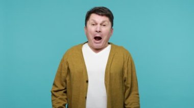 Beyaz tişörtlü ve hırkalı coşkulu olgun adam zaferini kutlarken eğleniyor, kazanmaktan şaşkına dönüyor. Mavi arka planda kapalı stüdyo çekimi