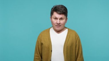 Son derece neşeli, misafirperver orta yaşlı adam el sallıyor merhaba diyor, sizi gördüğüme sevindim, dostça bir ifadeyle kameraya bakıyor ve gülümsüyor. Mavi arka planda kapalı stüdyo çekimi