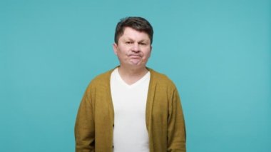 Daha fazla zamana ihtiyacım var! Tatminsiz, olgun, siyah saçlı, beyaz tişörtlü ve hırkalı bir adamın el hareketleriyle mola vermesi gerekiyor. Mavi arka planda kapalı stüdyo çekimi