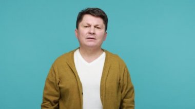 Bu konu hakkında bir şey duymak istemiyorum! Gergin, olgun bir adamın elleriyle kulaklarını kapatması, dinlemeyi reddetmesi, çatışmadan kaçınması, sorunları görmezden gelmesi. Mavi arka planda kapalı stüdyo çekimi