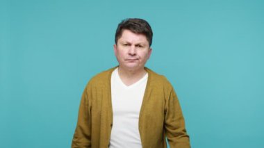 Tehlikeli, orta yaşlı, orta yaşlı, koyu saçlı, boynuzlarını göstererek el ele tutuşan saldırgan bir şekilde kameraya bakan ve saldırmaya hazır bir adam. Mavi arka planda kapalı stüdyo çekimi