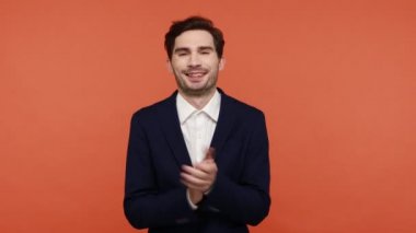 Zarif siyah iş elbisesi içinde sakallı neşeli, pozitif sakallı adam alkışlıyor, performansını alkışlıyor, mutlu görünüyor, bravo. Turuncu arka planda kapalı stüdyo çekimleri.