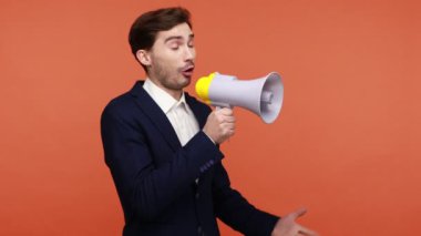 İş elbisesi içinde sakallı aktif bir adam megafonda yüksek sesle konuşuyor, dikkat ediyor ve barışçıl bir protesto yapıyor, önemli bilgiler veriyor. Turuncu arka planda kapalı stüdyo çekimleri