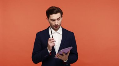 Resmi tarz takım elbiseli dalgın sakallı işadamı plan ya da görev listesi yapar. Kalemle not alır, program hazırlar. Turuncu arka planda kapalı stüdyo çekimleri