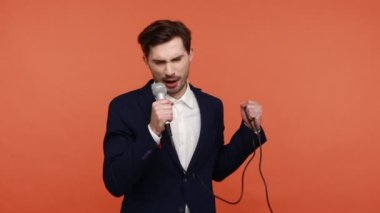 Duygusal sakallı yetenekli iş adamı karaokede duygusal bir şarkı söylüyor, mikrofonu elinde tutuyor, en sevdiği şarkıyı söylüyor, yaratıcılık. Turuncu arka planda kapalı stüdyo çekimleri