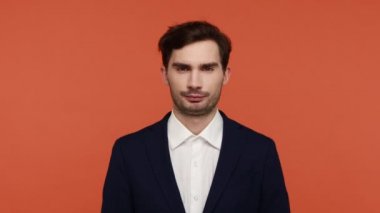 Siyah takım elbiseli, elinde yeşil elma ve şekerli donut tutan kendine güvenen sakallı bir adam sağlıklı yemek ve sağlık hizmeti kavramı için çağrıda bulunuyor. Turuncu arka planda kapalı stüdyo çekimleri.