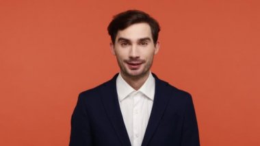 Resmi tarzda giyinmiş mutlu sakallı bir adamın portresi, kamerayı işaret eden, seni seçen, iyi haberler hazırlayan, neşeli bir olay gösteren. Turuncu arka planda kapalı stüdyo çekimleri.