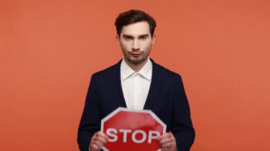 Ciddi sakallı iş adamının portresi resmi kıyafet giyer ve kırmızı trafik işaretini gösterir, uyarır ve tetikte olmak ister. Turuncu arka planda kapalı stüdyo çekimleri