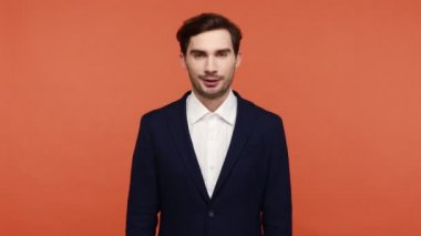 Hey sen, ara beni! Sakallı genç işadamı parmaklarını kulağına yakın tutuyor telefon hareketlerini gösteriyor, geri arıyor, iletişim kuruyor. Turuncu arka planda kapalı stüdyo çekimleri