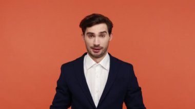 Sakallı, neşeli, resmi tarzda giyinmiş, ev tabelası takmış, başını sokacak bir çatı jesti yapmış, kibarca gülümseyen, güvende hisseden genç bir adam. Turuncu arka planda kapalı stüdyo çekimleri.