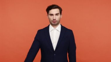 Evet, efendim! Vatansever, takım elbiseli ciddi bir adam el ele tutuşup selam veriyor, sorumluluk sahibi bir ifade takınıyor, disiplinli bir erkek çalışanın emirlerini dinliyor. Turuncu arka planda kapalı stüdyo çekimleri.