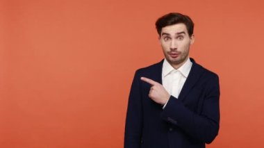 Reklamlara dikkat! Siyah takım elbiseli duygusal olarak şaşırmış bir adam, reklam metinleri için fotokopi alanı gösteriyor, şok edici haberler. Turuncu arka planda kapalı stüdyo çekimleri
