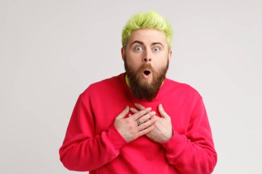 Süveter giymiş, ağzı açık duran, ağzı açık şaşırmış, şok olmuş, inanılmaz haberler duyan, elleri göğsünde şaşırmış bir adamın ön görüntüsü. Gri arka planda izole edilmiş kapalı stüdyo görüntüleri.