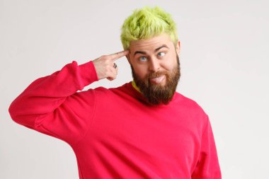 Yakışıklı, sakallı, elinde tabanca figürü, parmakları şakaktan şakağa, şaşı gibi şaşı bakıyor, rutinden yorgun, kırmızı kazak giyiyor. Gri arka planda izole edilmiş kapalı stüdyo görüntüleri.