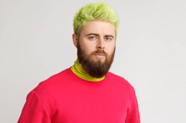 Beyaz sakallı yakışıklı bir adamın portresi, doğrudan kameraya bakıyor, katı ve ciddi bir yüz ifadesi var, günlük kıyafetler giyiyor. Gri arka planda izole edilmiş kapalı stüdyo görüntüleri.