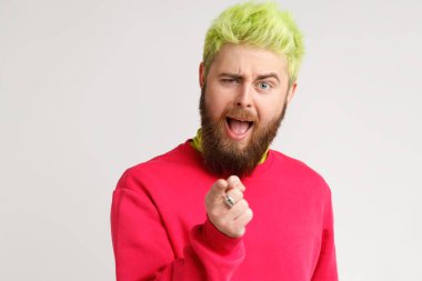 Şaşırmış, sakallı, parlak saçlı, kırmızı kazaklı, kamerayı işaret eden sorgulayıcı bir ifadeyle, göz kırpan gözlerle bakan bir adam. Gri arka planda izole edilmiş kapalı stüdyo görüntüleri.