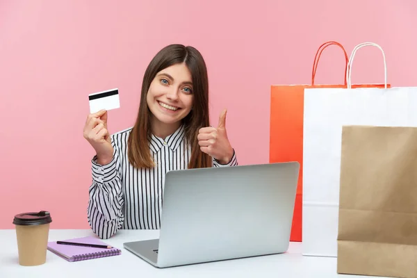満足笑みを浮かべて女性が親指を表示し 手にクレジットカードを保持し 簡単にオンラインショッピングと高速購入配信に満足 ピンクの背景に隔離された屋内スタジオショット — ストック写真