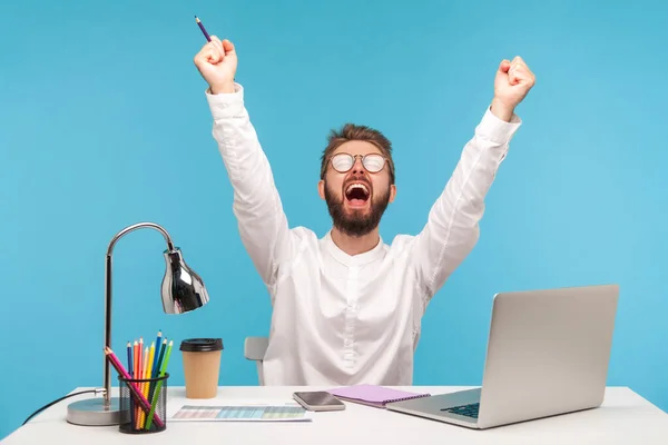 Very excited man with beard office worker screaming eureka raising hands up, solving hard task, getting access, successfully completing work. Indoor studio shot isolated on blue background
