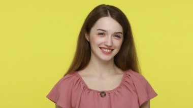 Sevimli kahverengi saçlı kadın neşeyle göz kırpıyor, kameraya gülümsüyor, flört ediyor ve göz kırpıyor, neşeli bir şekilde neşeleniyor. Sarı arka planda kapalı stüdyo çekimleri.