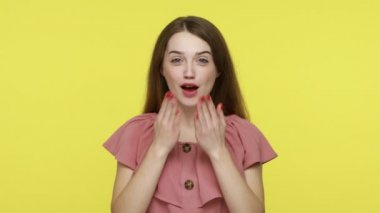 Genç, çekici, mutlu, kahverengi saçlı kadın kameraya sevgiyle bakıyor, şehvetli öpücükler yolluyor, romantik duygular ifade ediyor ve flört ediyor. Sarı arka planda kapalı stüdyo çekimleri.