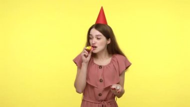 Kafasında parti konisi olan iyimser, neşeli bir kadın parti kornası ve konfeti simleri çalıyor, doğum gününü kutluyor, tebrik ediyor, neşeli bir ruh hali içinde. Sarı zemin üzerinde kapalı çekim izole