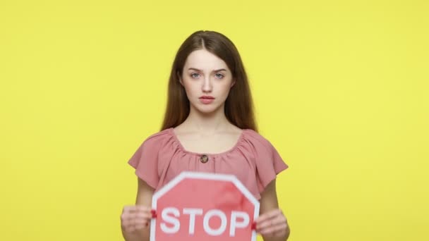 手の中に赤の停止記号を保持エレガントなピンクのドレスに深刻な集中女性は カメラを見て 危険性について警告し 悪い習慣を否定する 黄色の背景に隔離された屋内スタジオショット — ストック動画