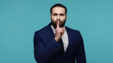 Sessiz ol, sırrını kimseye söyleme! Resmi stil takım elbiseli esmer adam ve sessiz kalmak istiyor. Mavi arka planda kapalı stüdyo çekimi.