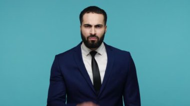 Siyah takım elbiseli ciddi bir hoşnutsuz adam uyarıda bulunuyor, onaylamıyor, hayır diyor, geri çekilmesini tavsiye ediyor. Mavi arka planda kapalı stüdyo çekimi.