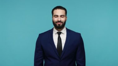 Resmi takım elbiseli neşeli, düşünceli, sakallı adam ilham verici bir ifadeyle hayal kuruyor, fantezi kuruyor ve düşünüyor, mutlu ve heyecanlı görünüyor. Mavi arka planda kapalı stüdyo çekimi.