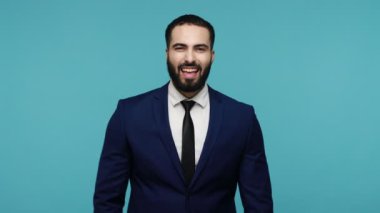 Ben kazandım! Son derece mutlu sakallı iş adamı sevinçle bağırıyor, muzaffer bir jestle yumruklarını kaldırıyor, mutlu bir şekilde bağırıyor, başarıyı kutluyor. Mavi arka planda kapalı stüdyo çekimi.