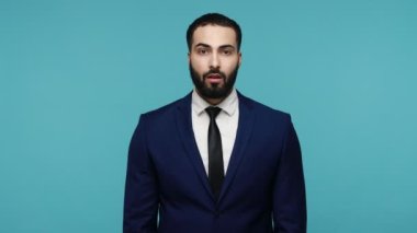 Takım elbiseli mutlu sakallı adamın başarılı bir zafere inanamamasına şaşıyorum. Büyük gözlerle kameraya bakıp, şok olmuş yüz ifadesi takınıyorum. Mavi arka planda kapalı stüdyo çekimi.
