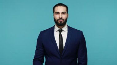 Resmi stil kıyafetli mutlu adam zafer işareti işareti gösteriyor, dişlek gülümsemeli kameraya bakıyor, kazanan, başarıyı kutlayan. Mavi arka planda kapalı stüdyo çekimi.