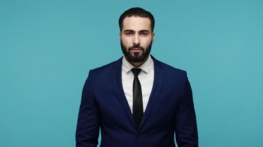 Hey, buraya bakın, abone olmak için tıklayın. Siyah takım elbiseli yakışıklı sakallı adam iki eliyle aşağıya bakıyor ve kameraya bakıyor. Mavi arka planda kapalı stüdyo çekimi.