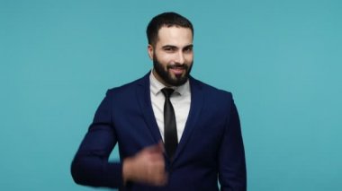 Bizimle irtibata geç. Siyah takım elbiseli genç, pozitif, sakallı, esmer bir adam, parmaklarını kulağına yakın tutuyor. Çağrı işareti yapıyor, aramaktan çekinmeyin, merkezi arayın. Mavi arka planda kapalı stüdyo çekimi.