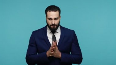 Endişeli, sakallı, tırnaklarını yiyen, gergin, kasvetli yüzüyle poz veren çekici bir adam ağlamak üzere. Mavi arka planda kapalı stüdyo çekimi.