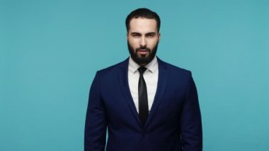 Takım elbiseli, sakallı, küçük parmak hareketi yapan, küçük boy veya görünmez nesne gösteren esmer bir adam. Düşük ölçekli, daha fazlasına ihtiyacı var. Mavi arka planda kapalı stüdyo çekimi.