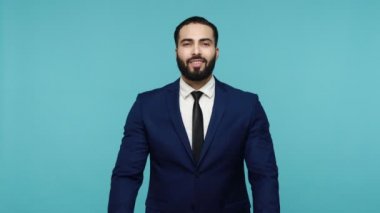 Kollarıma gel! İyi huylu esmer, siyah takım elbiseli, sakallı, mutlu bir şekilde gülümseyen ve kucaklaşmak için elini kaldıran bir adam. Sizinle tanıştığıma çok memnun oldum. Mavi arka planda kapalı stüdyo çekimi.