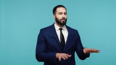 Siyah takım elbiseli, siyah sakallı, engellere uzanmış elleriyle dokunmaya çalışan, yolu göremeyen, yolunu kaybetmiş bir adam. Mavi arka planda kapalı stüdyo çekimi.