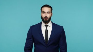 Yemin ederim! Sorumlu, siyah takım elbiseli genç ve ciddi bir iş adamı elini kaldırarak söz veriyor ve onaylayıcı bir şekilde dürüst bir adama söz veriyor. Mavi arka planda kapalı stüdyo çekimi.