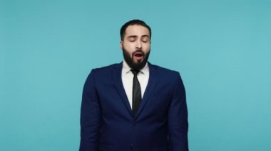 Uykulu, yorgun, resmi takım elbiseli sakallı adamın dinlenmeye ihtiyacı var. Geniş esneme hissi uykulu yorgunluk, zor uyanma, uykusuzluk kronik yorgunluk sendromu. Mavi arka planda kapalı stüdyo çekimi.